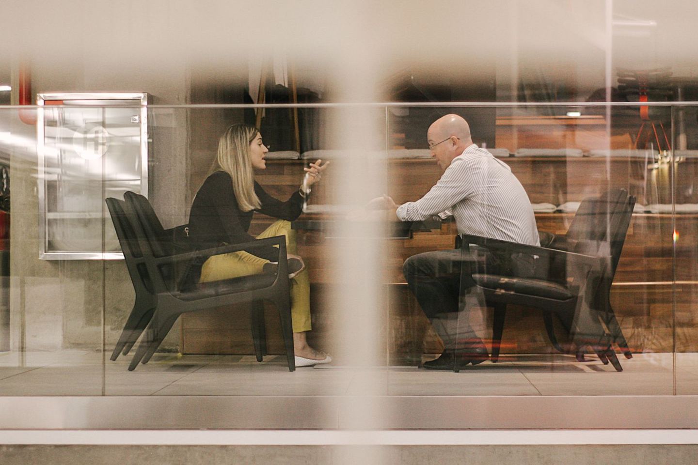 Two professionals in a focused one-to-one discussion inside a glass meeting room